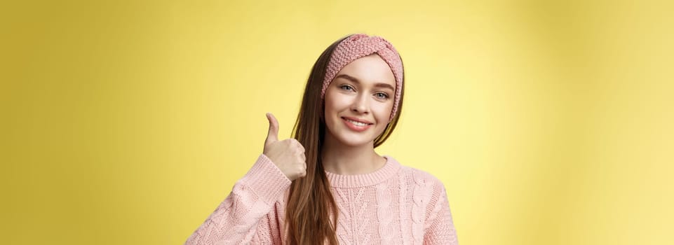 Pretty european young girl in headband, pink sweater smiling delighted, pleased showing thumbs up in agreement, approval, giving good recommendation, liking interesting great idea smiling cheerful.