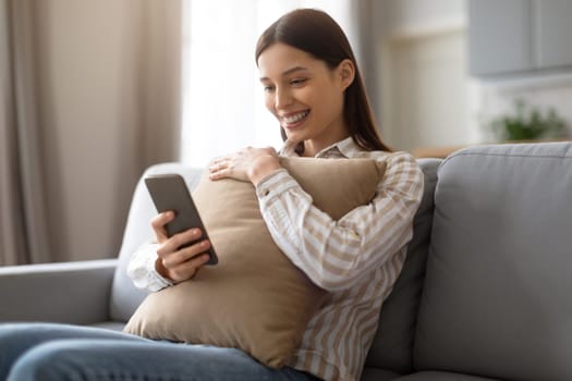 Smiling woman relaxing with phone and cushion on sofa