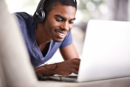 Man, face and music with laptop in home for internet streaming, podcast and online research with smile. Student, black person and technology with headphones for relax, studying and learning on couch.
