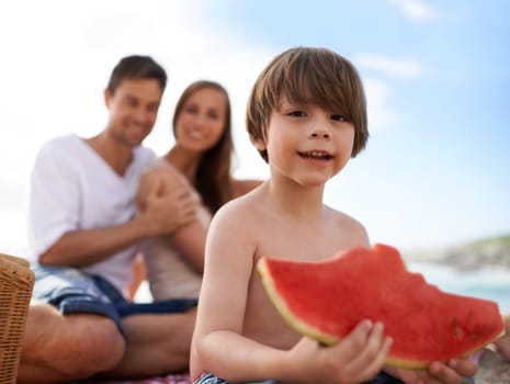 Portrait, parents and kid on beach with watermelon, picnic and tropical holiday in Australia. Mother, father and happy face of boy child relax at ocean with sunshine, eating fruit and smile in summer