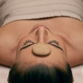 Massage, spa and stone on head of woman on table to relax with stress relief or luxury treatment. Calm, wellness and zen with young beauty customer on table for balance, inner peace or mindfulness