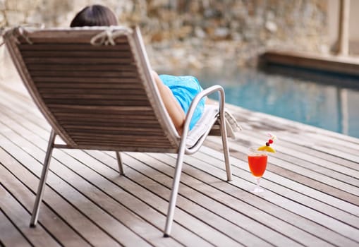 Deckchair, woman and cocktail at poolside for holiday or getaway on weekend in summer. Rear view and break with alcohol beverage or juice for refresh and relax on vacation, resort or lodge to tan