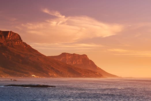 Ocean, sunset and clouds on mountains by blue sky and outdoor travel for vacation in nature. Landscape, sea and sunlight on false bay with calm and seal island in cape town for tourist destination