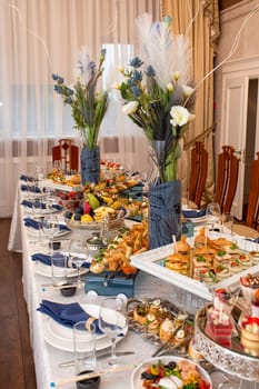 Opulent buffet with snacks, sandwiches, fruits, sweets on decorated table with blue accents.