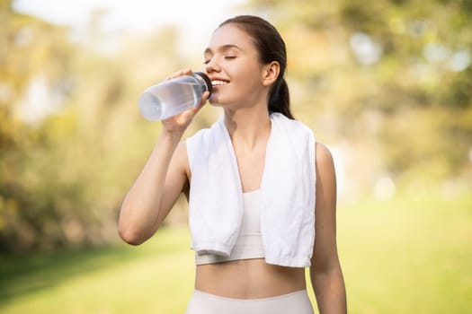 A joyful young woman quenches her thirst by drinking water from a clear bottle