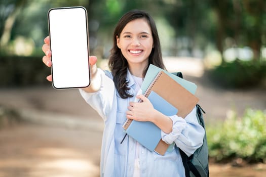 A cheerful young student shows her smartphone screen while holding textbooks