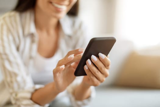 Unrecognizable Woman Using Modern Smartphone While Sitting On Couch At Home, Closeup Shot Of Female Hands Holding Cellphone, Young Woman Browsing App On Mobile Phone Or Shopping Online, Cropped
