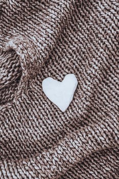 A beautiful background of a nice brown knitted sweater with a small decorative white heart on it. Conceptual photo of love and warmth.