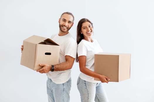 Cheerful millennial couple carrying cardboard boxes, packing stuff for relocation
