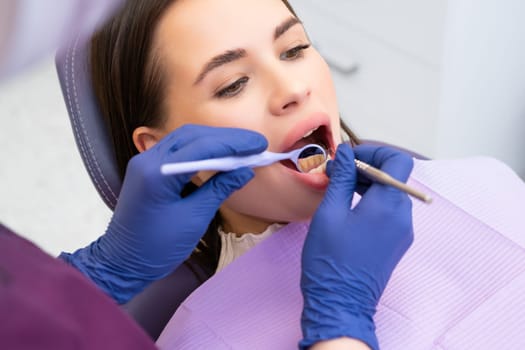 Over the shoulder view of a dentist examining a female patients teeth in dental office.