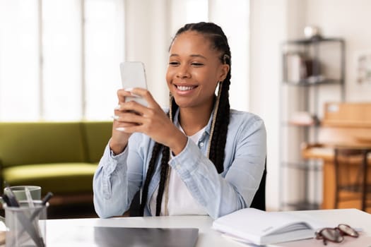 Delighted black teenage lady using her smartphone, chatting with friends online