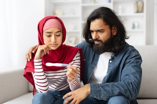 Infertility Problems. Upset Young Muslim Couple Looking At Negative Pregnancy Test