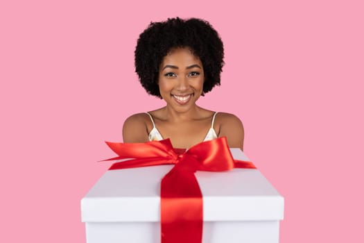 Enthusiastic African American woman with a joyful smile presenting a large white gift box