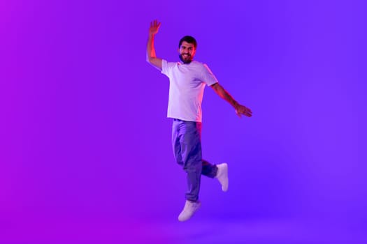 carefree man jumps raises arm posing in mid air, studio