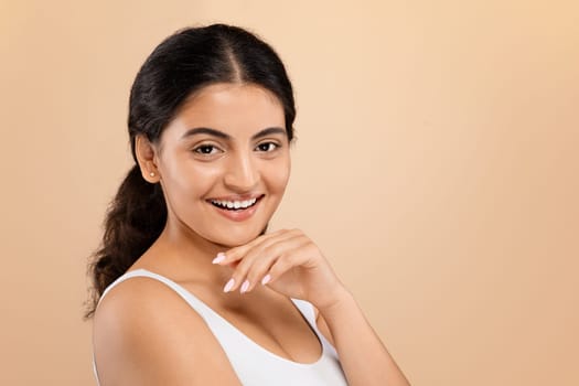 Beautiful indian woman in sleeveless top touching chin and smiling at camera