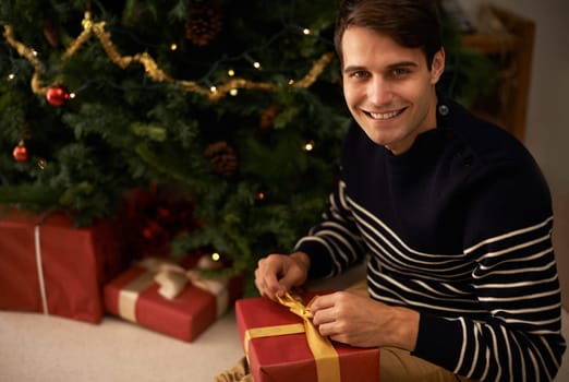 Portrait, Christmas tree and man wrapping box in home for preparation of holiday event of tradition. Gift, present and smile with happy young person in apartment for December celebration or vacation