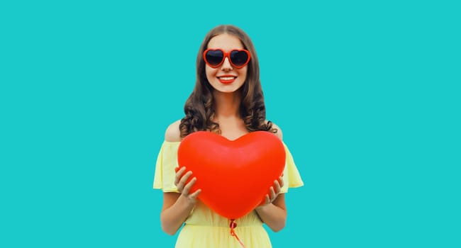 Happy smiling young woman with red heart shaped balloon on blue studio background