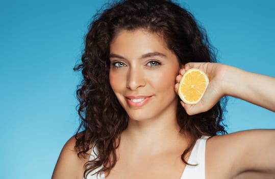 Smiling millennial caucasian lady hold orange, enjoy beauty care, isolated on blue studio background, close up. Recommendation vitamin c, procedures for skin, natural cosmetics