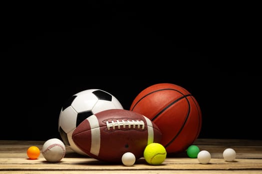 Set of various sport balls on wooden floor on black background close up