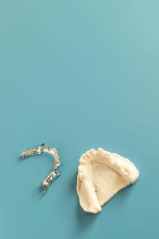 Metal Frame Lower Partial Denture with Die Stone, Plaster Cast Molds Of Lower Jaws, Cobalt Chrome Dental Plate, Flat Lay Mockup 3D Printed Bridge On Blue Background. Copy Space. Vertical Plane.