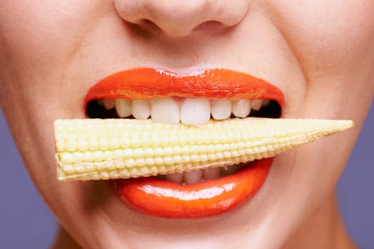 Woman, lipstick and vegetable in mouth for beauty, nutrition and healthy with vegan cosmetic product in studio. Cruelty free makeup, cosmetology and baby corn, orange lip gloss for aesthetic or art