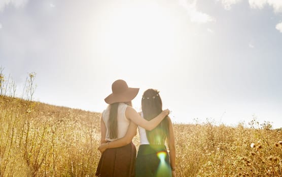 Friends, walking and hug in summer nature on holiday or journey on vacation for adventure. Women, back and embrace outdoor together in sunshine on field, trekking on hill or travel environment.