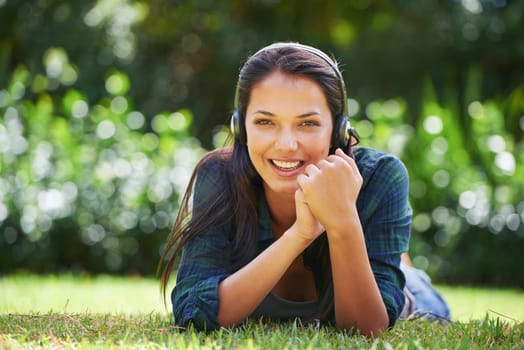 Music, headphones and relax for girl on grass outdoor in garden, lawn or forest for podcast, sound or streaming. Young person and smile with gadget in nature or tranquil environment in spring