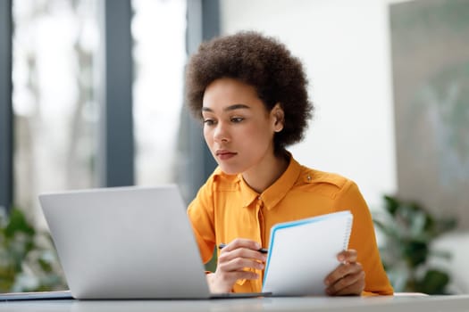 Focused young black woman studying with laptop and notebook