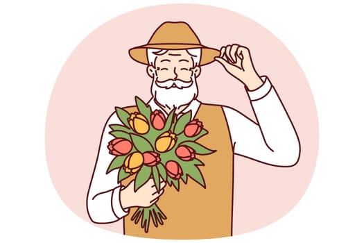Cheerful elderly man with beard holds bouquet of spring flowers touches hat in greeting