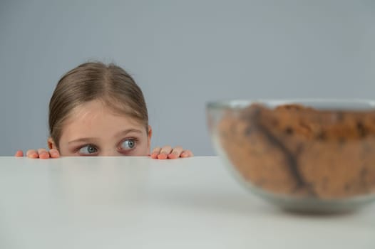 A little girl tries to steal cookies from the table.