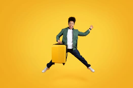 Excited african american guy traveler jumping with suitcase