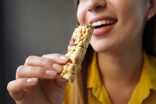 Young woman eating a nuts cereal bar without sugar on gray background