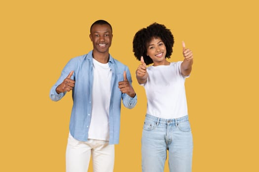 Happy African American couple giving thumbs up, with the man in a blue shirt and white pants