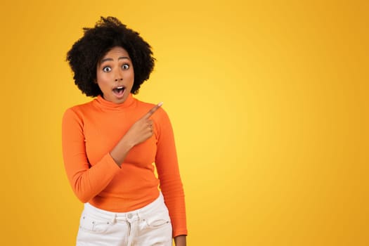 Shocked African American woman with curly hair pointing to the side, mouth open in surprise