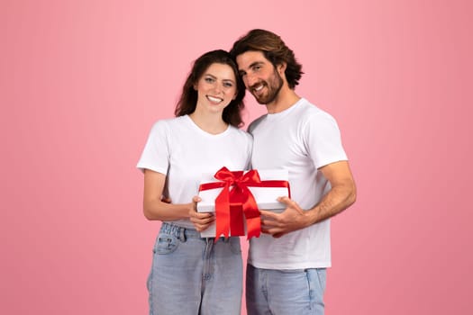 Smiling young couple in casual white t-shirts sharing a special moment with a man giving a white gift box