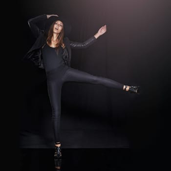 Portrait, fashion and balance with woman on black background in studio for clothing dance. Leather, model and outfit with confident young person in dark clothes for chic, edgy or trendy style.
