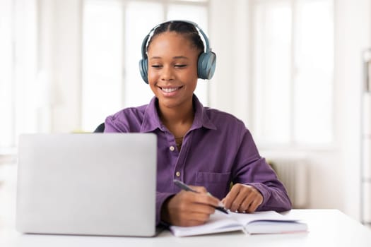 Lady student with headphones taking notes during an online class