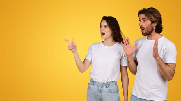 Amazed couple in white t-shirts gesturing with excitement, the woman pointing to the side