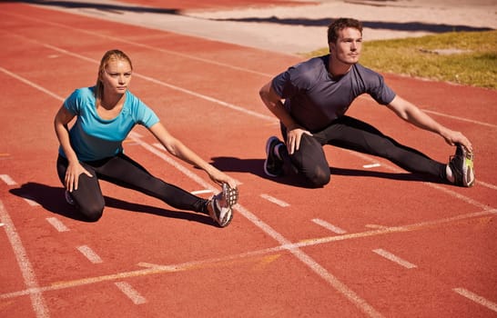 Training, legs and couple stretching in stadium for race, marathon or competition for health. Sports, fitness and runner athletes with warm up exercise for running cardio workout on outdoor track.