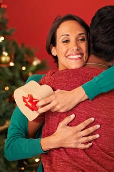 Friends, hug and Christmas with surprise, gift box and celebration on red studio background. Face, people or woman with Xmas present or parcel with embrace or excited with package or bonding together.