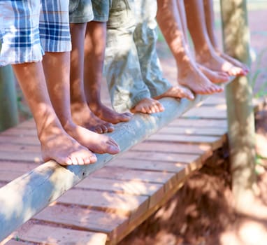 Children, feet and closeup of balancing on wood in nature for fun and adventure. Legs, zoom and diverse kids playing outside on tree with stability and support for development and friends bonding