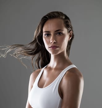 Woman, serious in portrait and confidence for fitness, strong and determined with sweat from workout on grey background. Hair in wind, athlete for sports and exercise with pride and power in studio