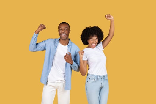 Enthusiastic African American couple celebrating success with arms raised and fists clenched