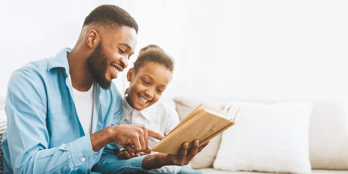 Caring african-american daddy reading book to his cute daughter, spending time at home