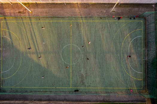 Aerial drone top view of mini football soccer field with artificial plastic cover with playing people. Public sport ground in city at sunny summer day drone view. Mini soccer field for children