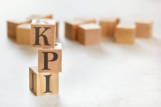 Three wooden cubes with letters KPI (means Key Performance Indicator), on white table, more in background, space for text in right down corner