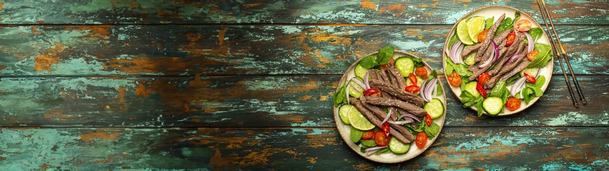 Two plates with traditional Thai beef salad with vegetables and mint top view served on rustic wooden background, healthy exotic asian meal