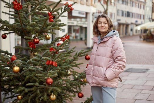 A beautiful girl stands on the street of the old European town of Bietigheim-Bissingen in Germany on Christmas Eve. Festive Fashion in the Heart of Europe. City streets are decorated with Christmas trees and New Year's decorations, tourism, fashion, historical places, Europe