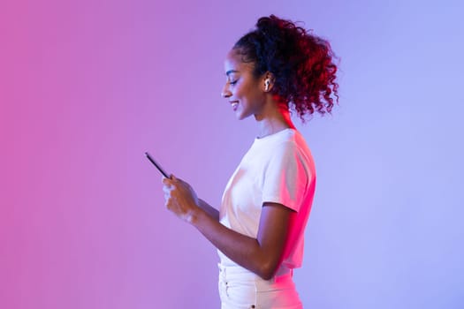 Happy black lady with smartphone and earbuds on pink and purple background