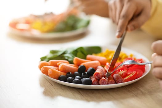 Selective focus on plate full of nutritive food vegetables, beans and meat. Unrecognizable man using fork and knife, eating breakfast or lunch, cutting sausage, cropped. Nutrition, healthy diet